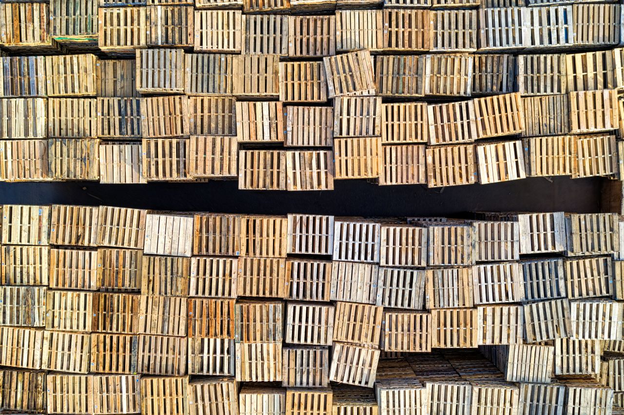High angle shot of neatly stacked wooden pallets in an outdoor warehouse setting.