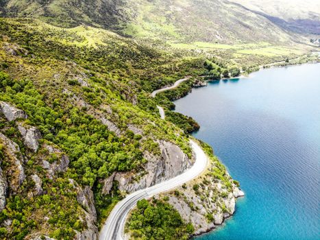 Stunning aerial capture of a winding road beside a tranquil lake with lush green hills.