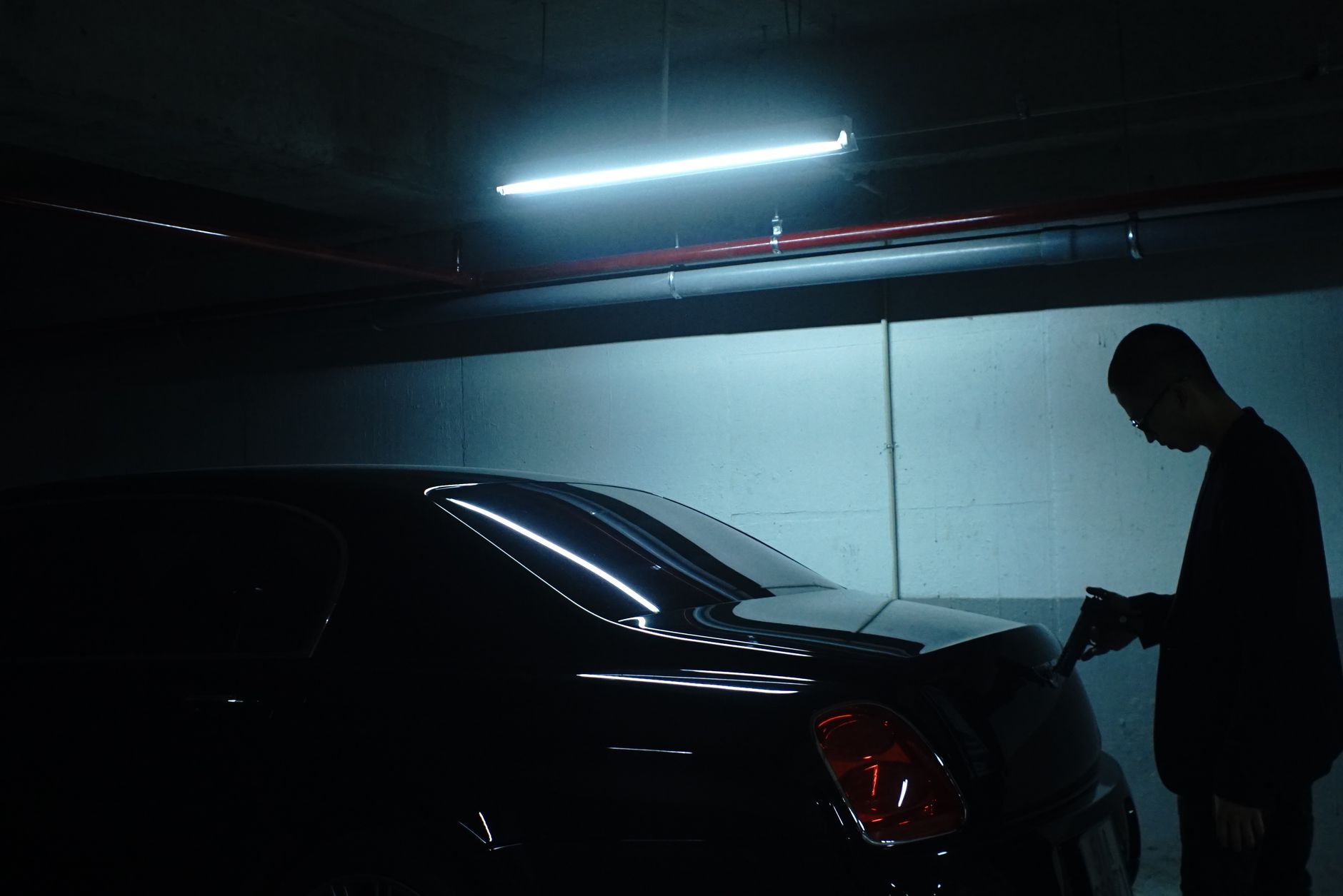 A dramatic silhouette scene in an underground parking lot in Vietnam, featuring a person and a parked car.