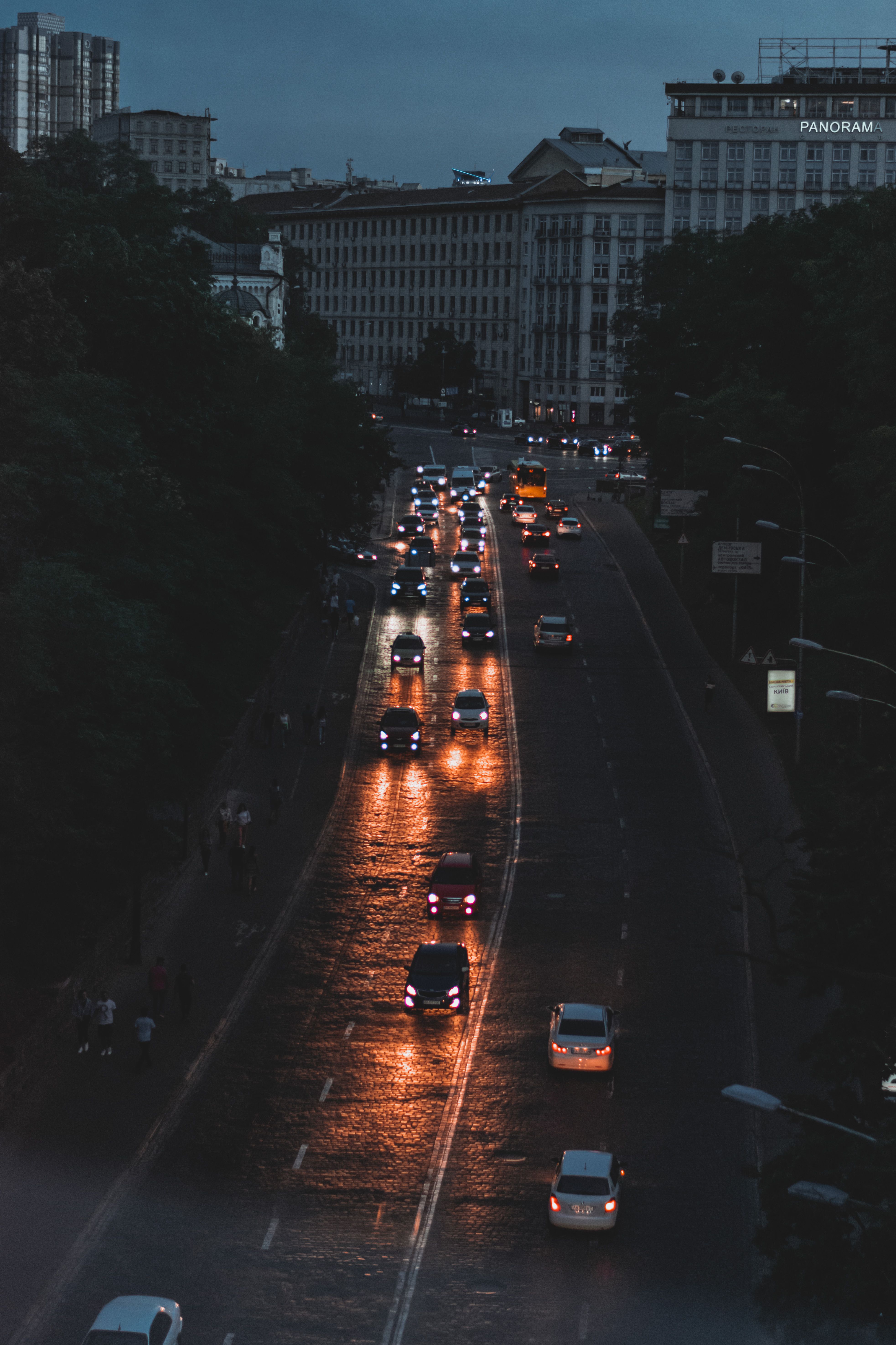 Cars navigating wet city streets at night, reflecting vibrant lights. Evening cityscape captured from above.