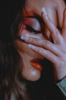 Close-up portrait of a woman with dramatic eye makeup and red lips, showcasing a stylish pose.