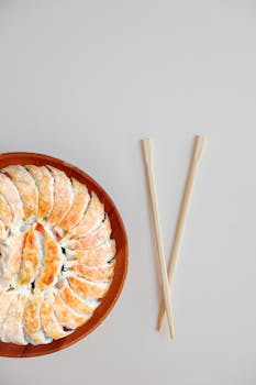 Top view of a plate of gyoza with chopsticks on a minimalist background.