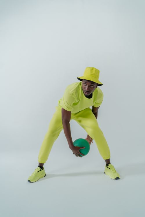 Free Full shot of a stylish man in bright outfit holding a green ball in a studio setting. Stock Photo