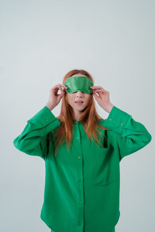 Free Portrait of a woman wearing a green sleep mask and matching pajamas in a studio setting. Stock Photo