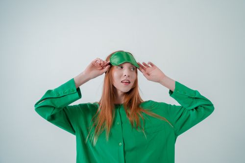 Free Portrait of a woman in a green shirt adjusting her sleep mask against a white background. Stock Photo