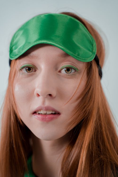 Free A close-up portrait of a woman with long red hair wearing a green eye mask and eye shadow. Stock Photo
