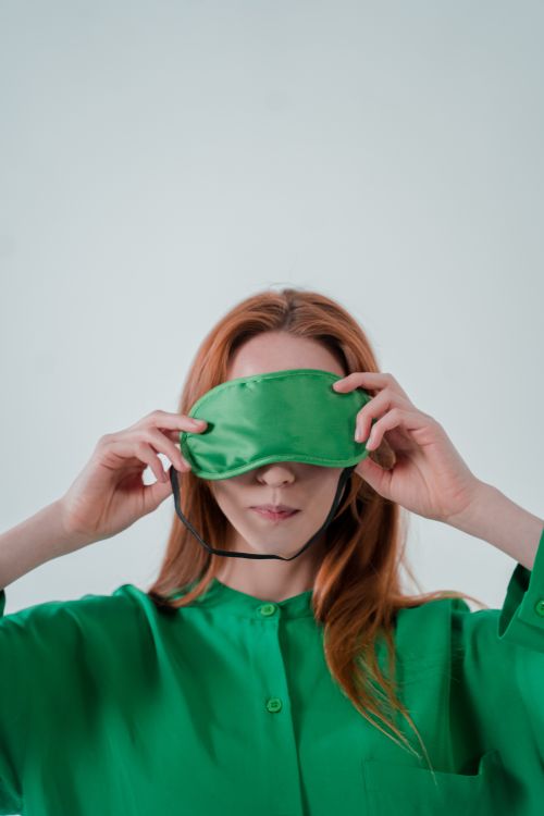 Free Portrait of a woman adjusting a green sleep mask against a plain background. Stock Photo