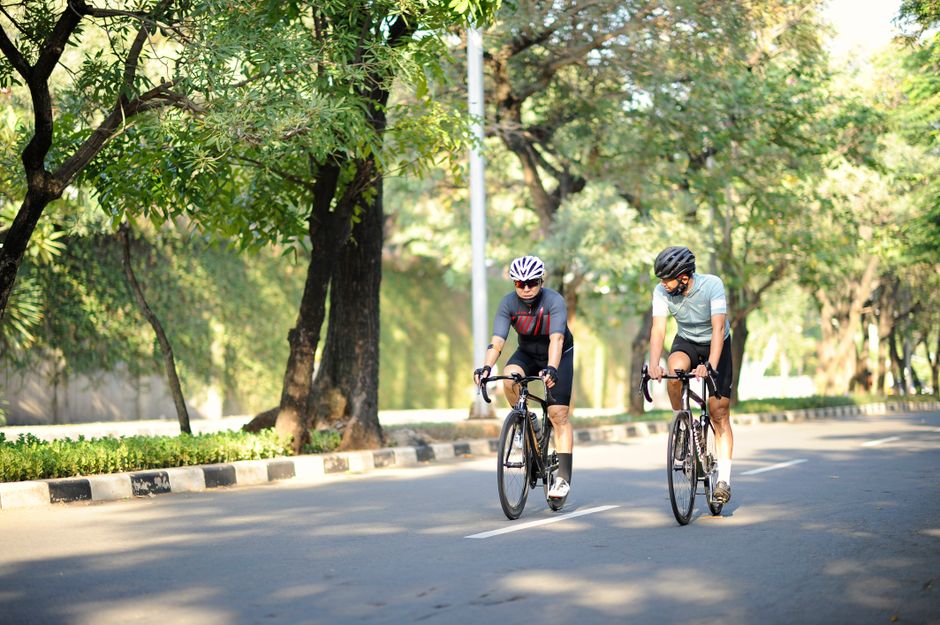 Two men cycling on a sunny day in a lush Jakarta park, embracing active lifestyles.