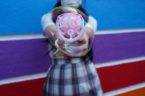 Free Close-up of a bubble blower creating bubbles against a multicolored wall background. Stock Photo