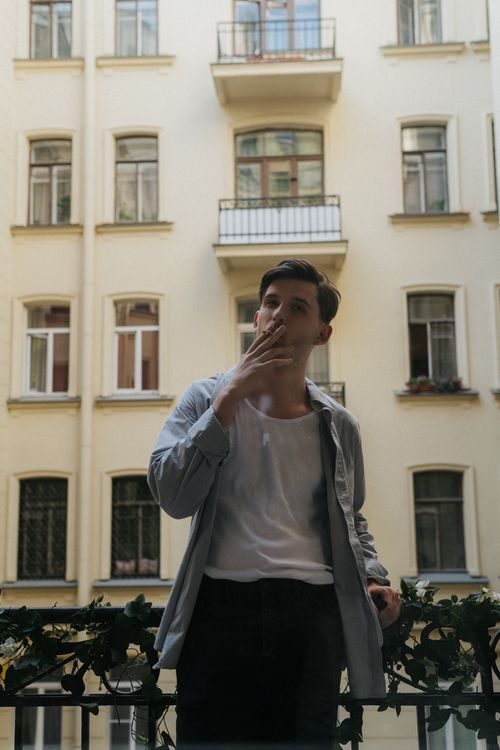 Free A young man stands outside smoking on a balcony of an urban apartment complex. Stock Photo