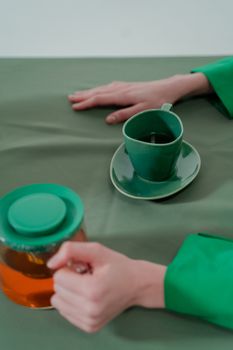 A serene composition featuring a green cup, teapot, and hands on a table, exuding calmness.
