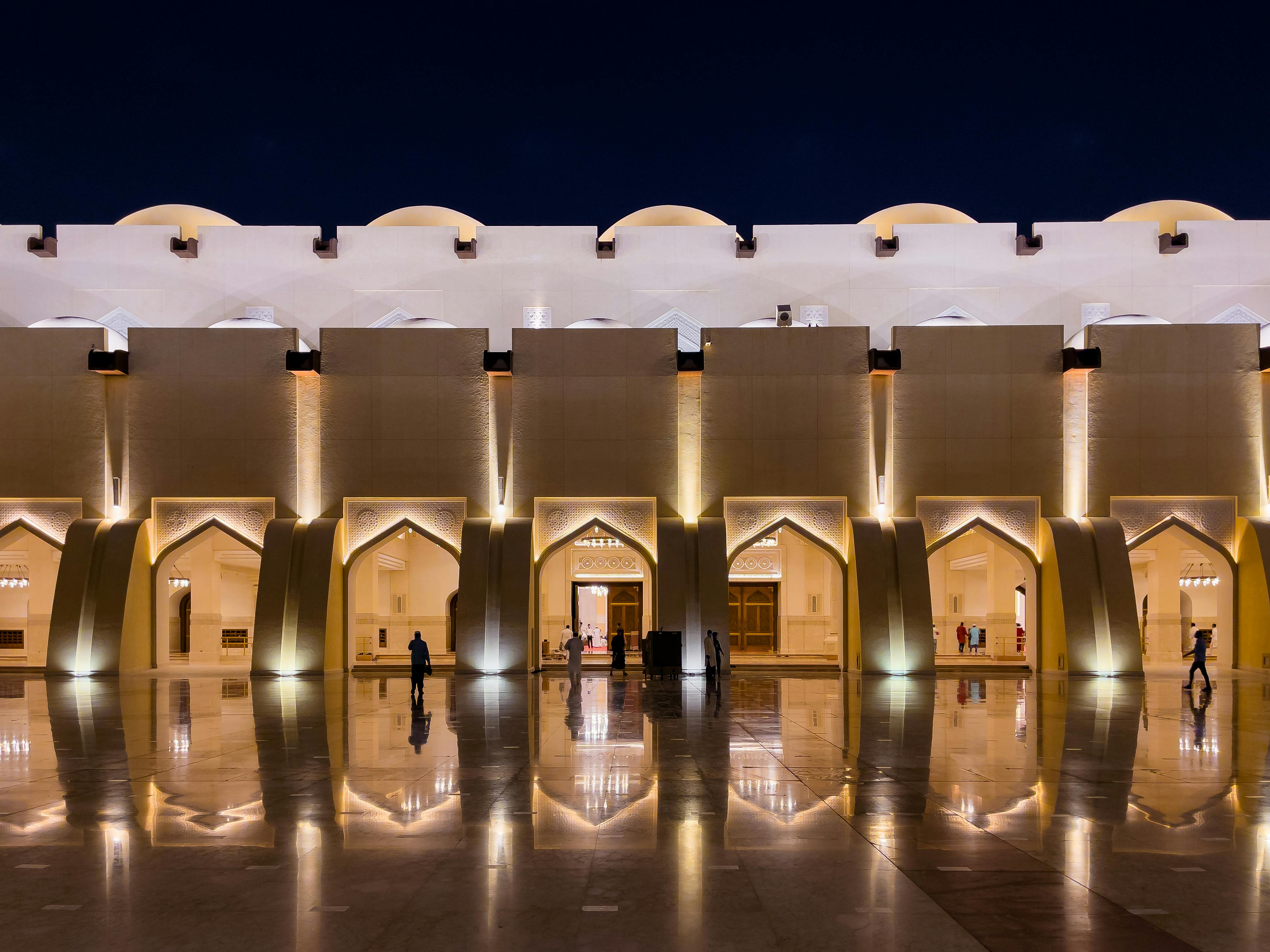 A beautifully illuminated mosque facade reflecting on a shiny surface in Doha, Qatar at night.