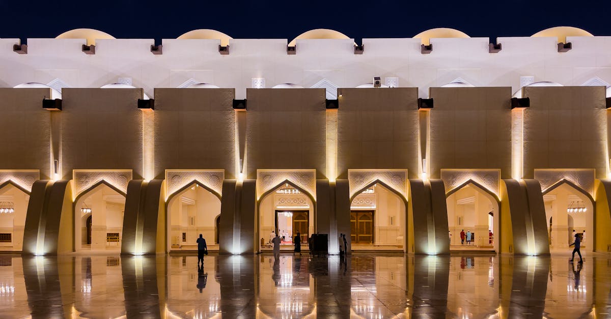 A beautifully illuminated mosque facade reflecting on a shiny surface in Doha, Qatar at night.