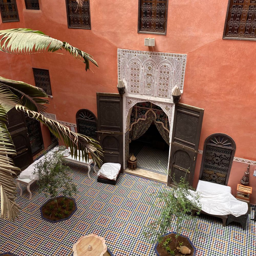 A terracotta-plastered courtyard room with a carved stucco doorway and zellige floor