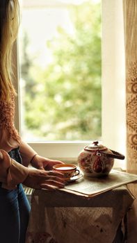 Embrace a serene moment with a cup of tea by a sunlit window, captured in a warm, relaxed setting.