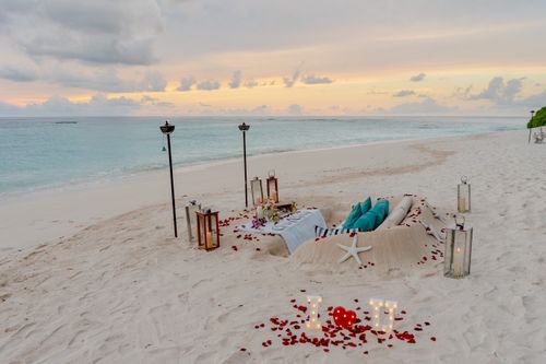 Free Intimate beach dining setup with glowing candles and ocean view at sunset. Stock Photo