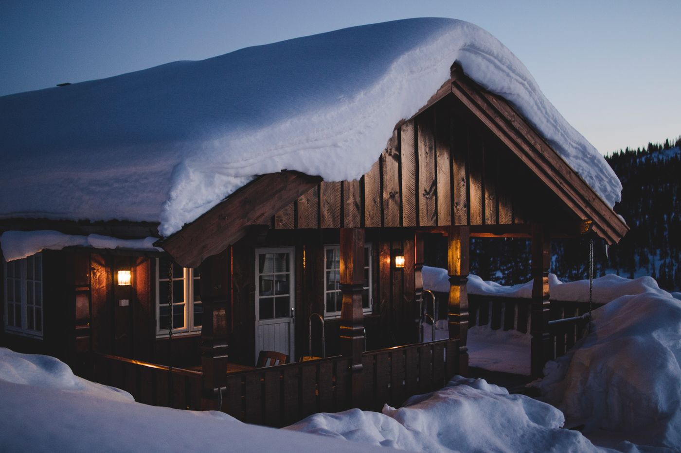 A snow-covered cabin glowing warmly against a winter dusk sky