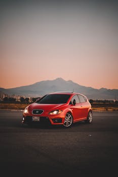 A sleek red sports car captured at dusk with a mountain backdrop, offering a dramatic and dynamic scene.