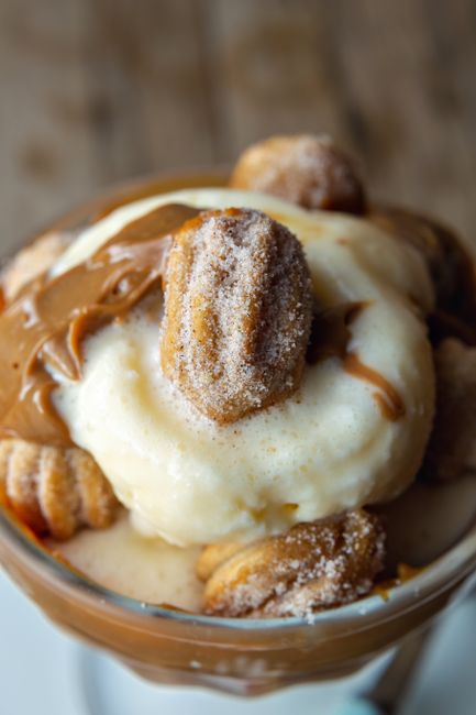 A glass bowl of pale golden milk curds cut into cubes, submerged in amber cinnamon syrup with a whole cinnamon stick resting across the top.