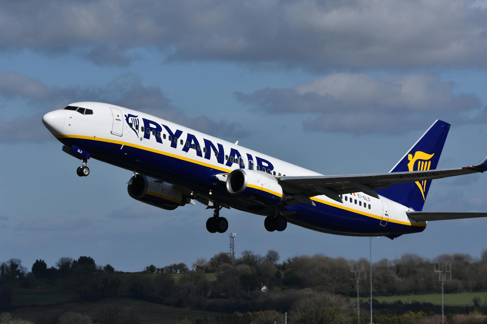 A Ryanair Boeing 737 aircraft taking off in a clear blue sky with background landscape.