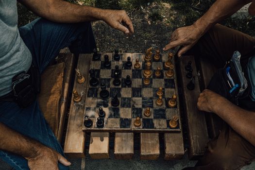 Two adults engaged in a strategic chess match on a rustic wooden board outdoors.