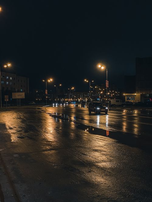 Free A moody nighttime street scene showcasing reflections on a wet road illuminated by streetlights. Stock Photo