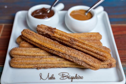 A plate of churros served with chocolate and caramel dips for a delightful treat.