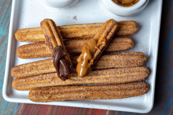 Cinnamon sugar churros on white platter, two dipped in chocolate and dulce de leche