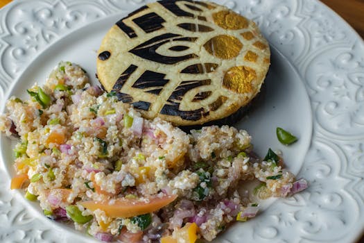 A close-up of a decorative eggplant slice paired with a colorful quinoa salad on a white ornate plate.