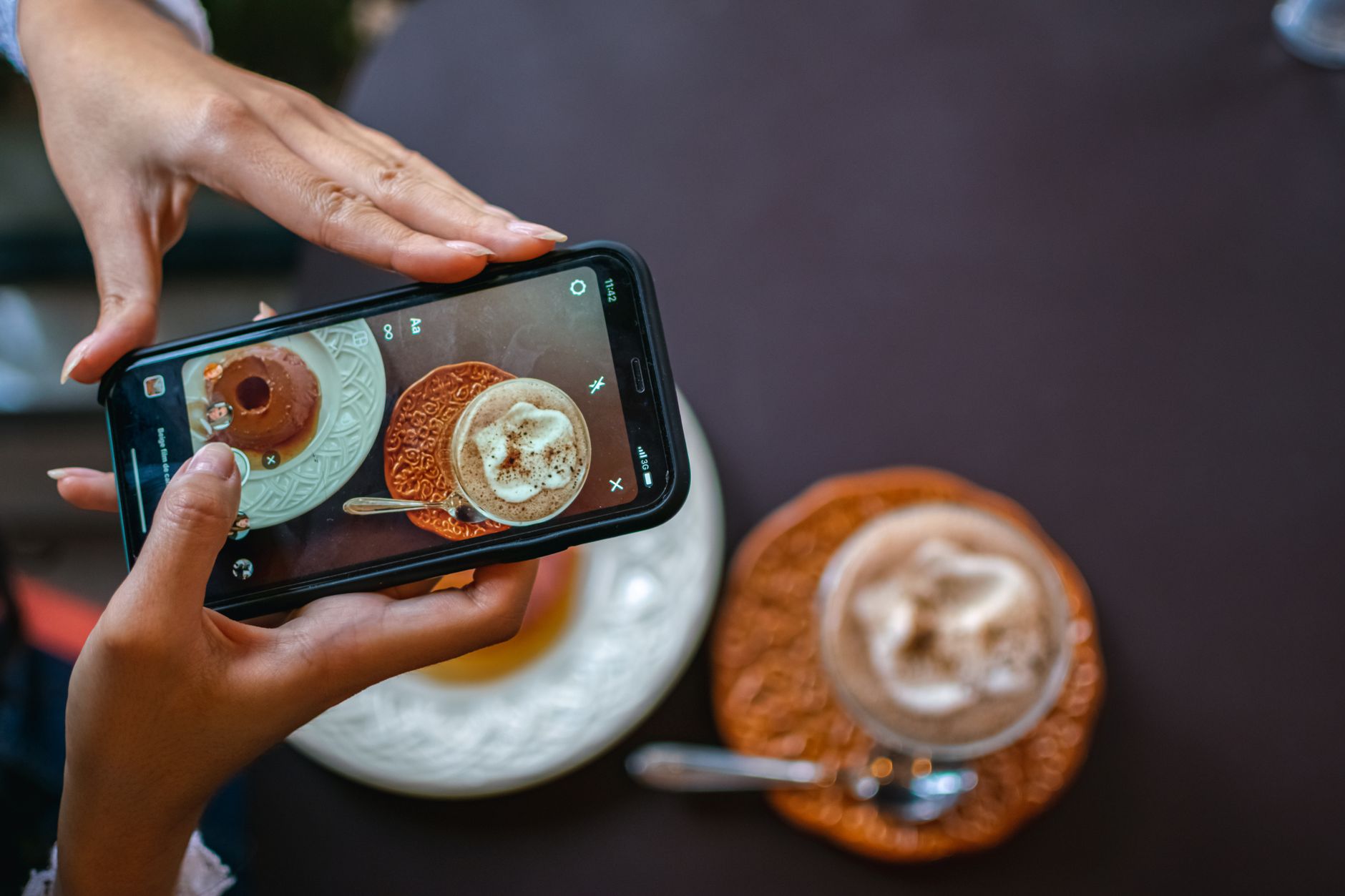 Mãos segurando um smartphone fotografando café e donut, ilustrando a criação de uma estratégia de UGC com tecnologia e comida