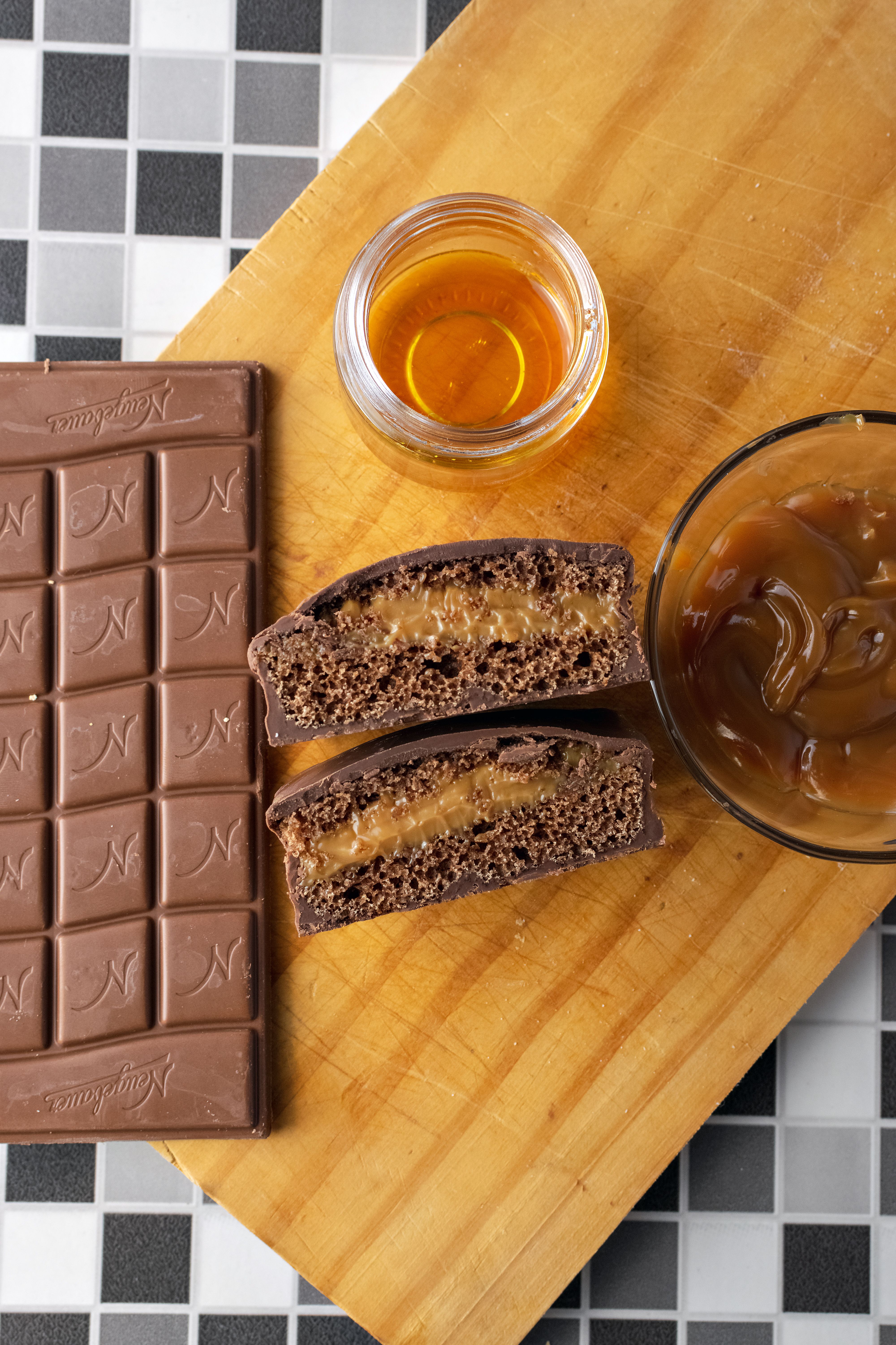 Flatlay of chocolate with caramel-filled pastries, honey, and a chopping board.