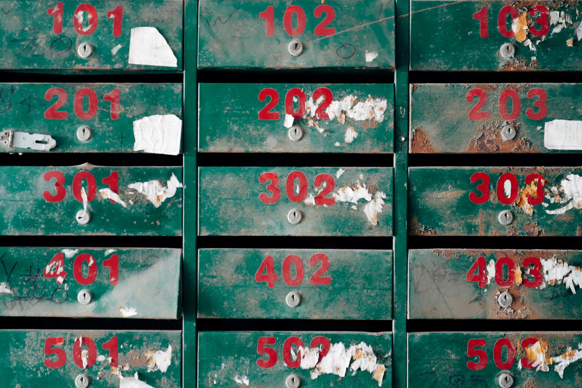 Old, rusty mailboxes with peeling paint and numbers, conveying neglect.