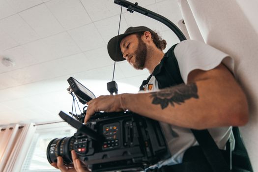 Bearded cameraman operating a professional camera indoors, focused on capturing the perfect shot.