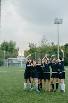 A joyful women's soccer team celebrates a victory outdoors on a soccer field.