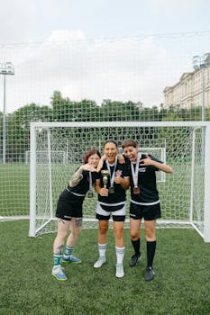 Joyful women footballers celebrating victory with medals on a soccer field.
