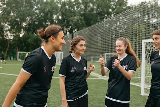 Group of female soccer players in black uniforms bonding outdoors, fostering teamwork.