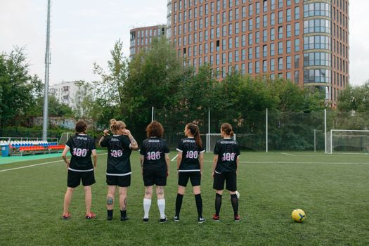 Back view of a women's soccer team preparing for match on an urban soccer field.