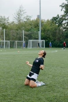 Caucasian woman celebrating on a soccer field, kneeling with joy. Perfect for sports and victory themes.