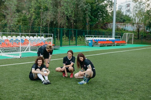 A Group of Girls in Uniform Sitting on Football Field