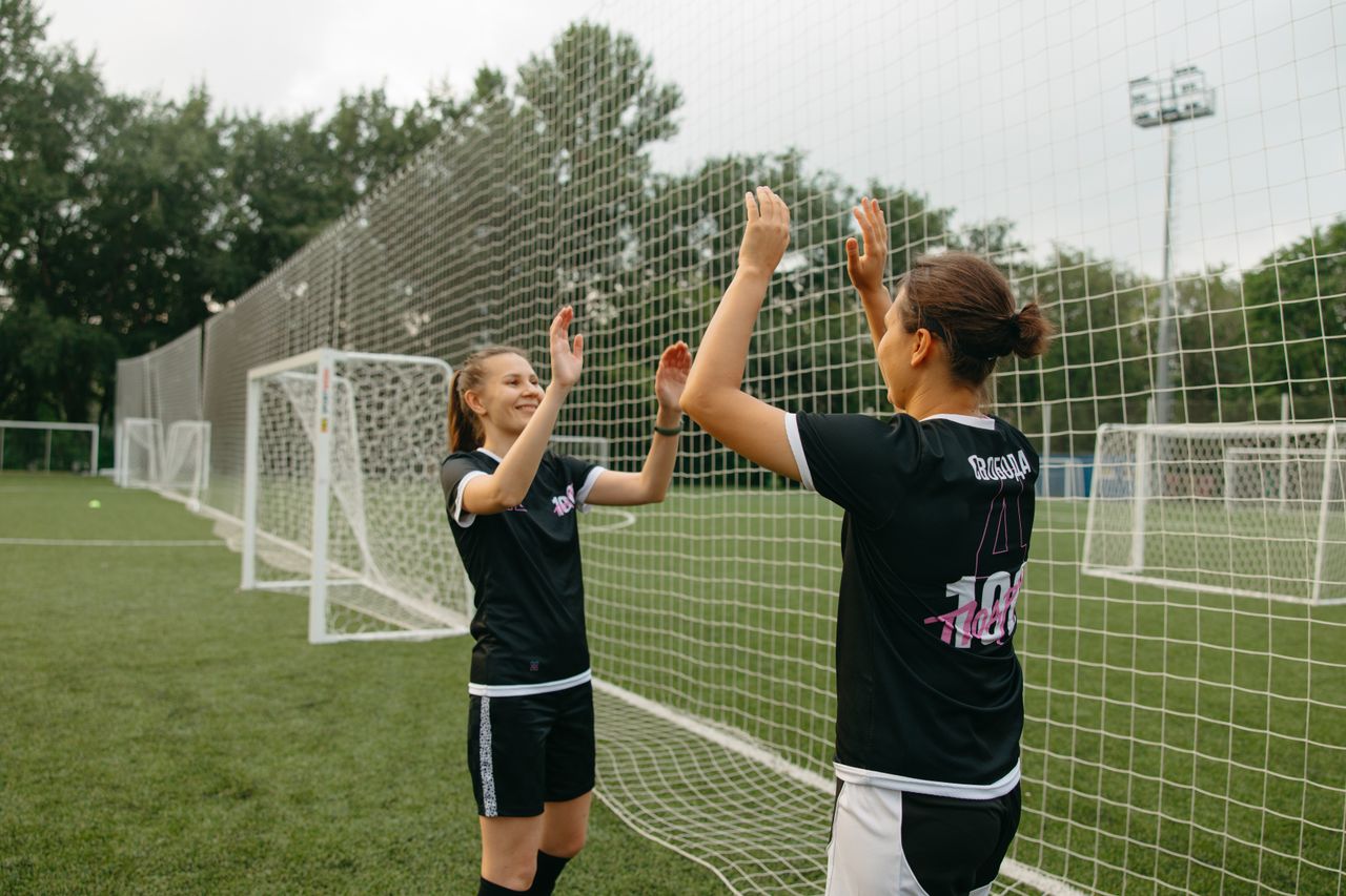 two women football players high fiving on a field celebrating teamwork