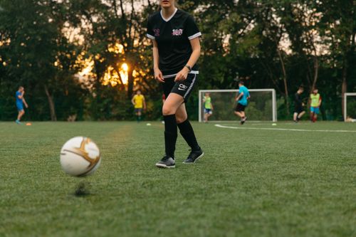 Free Female soccer player dribbling a ball during a casual game on a grassy field at sunset. Stock Photo