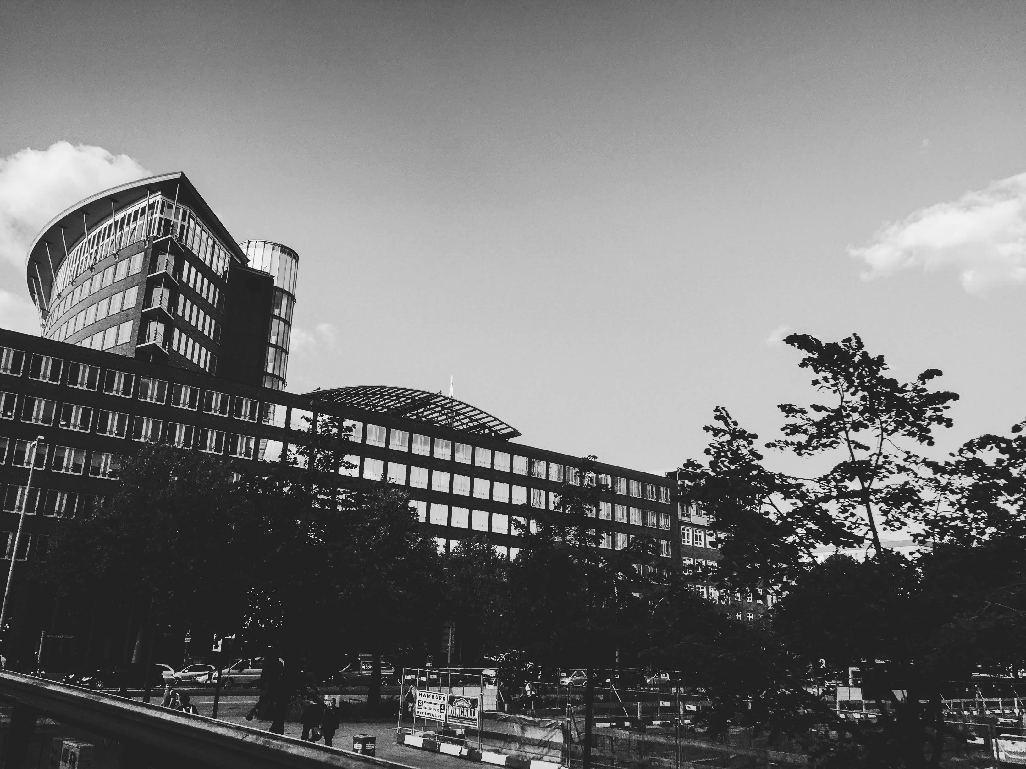 这张黑白照片展现了一座现代城市建筑，前景有树木，呈现了当代城市场景