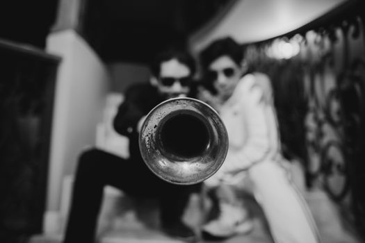 Intense black-and-white photo of a trumpet focused performance with two stylish individuals.