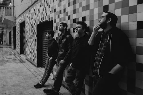 Monochrome Photo of Men leaning on the Wall 