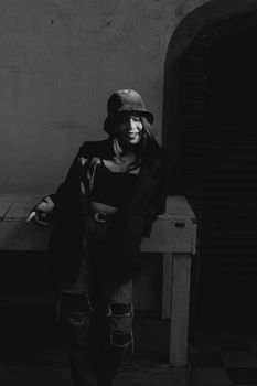 Stylish woman in bucket hat and jacket posing in monochrome lighting.