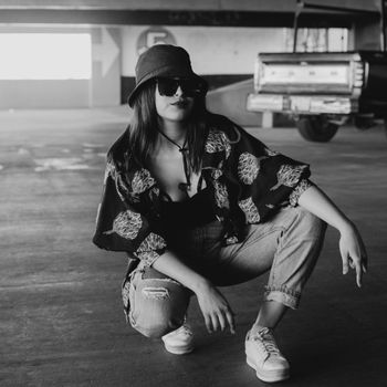 Monochrome portrait of a fashionable woman crouching in a parking lot.
