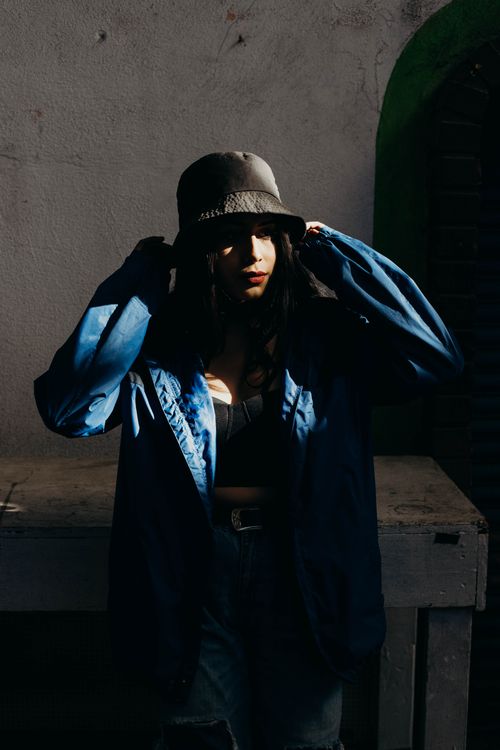Free Stylish woman in a bucket hat poses in urban shadows, showcasing edgy street fashion. Stock Photo
