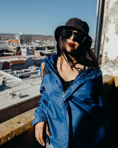 Free A fashionable woman in a blue jacket and sunglasses poses on a sunny urban rooftop. Stock Photo