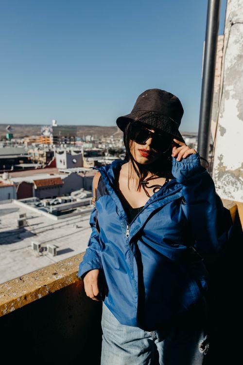 Free Stylish woman in a bucket hat and blue jacket poses outdoors with an urban skyline. Stock Photo