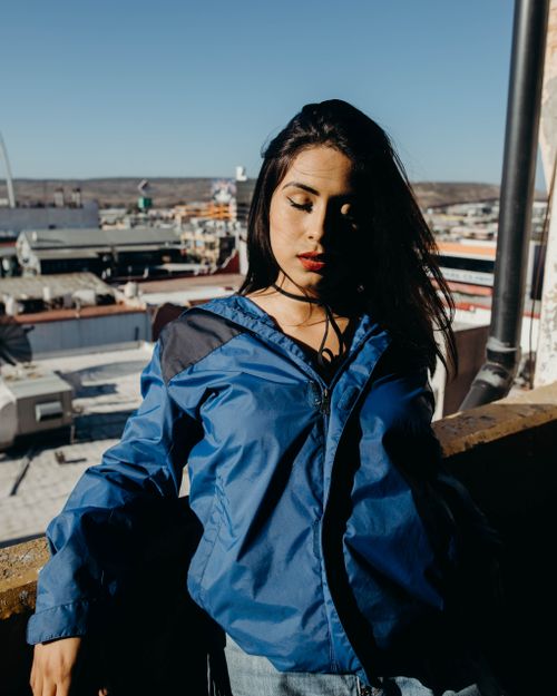 Free An adult woman in a blue jacket enjoys a sunny day on an urban rooftop. Stock Photo